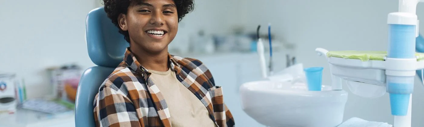 A smiling person seated in a dental chair with dental equipment in a clean clinic.